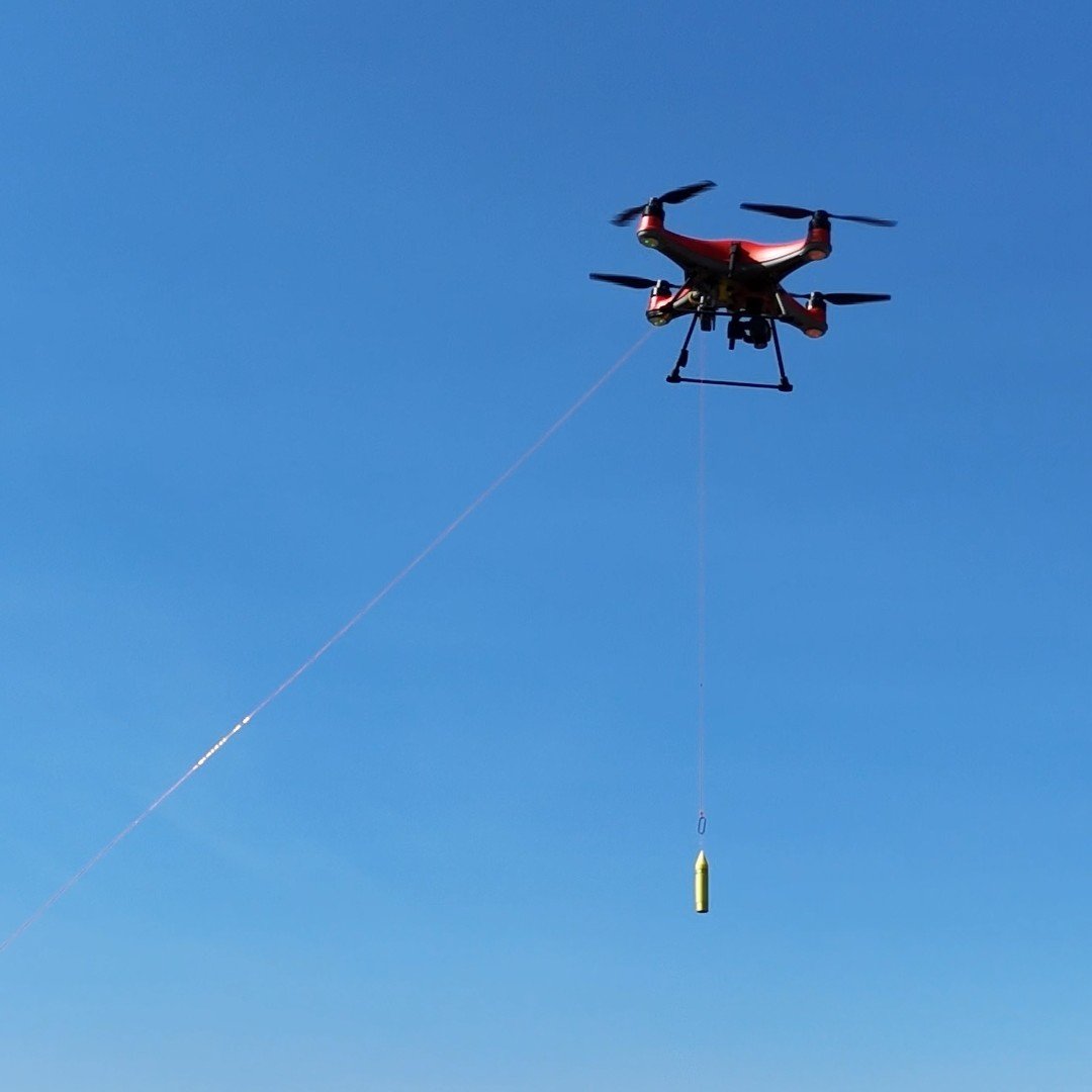 Drone Lyne carrying a suspended payload against the sky